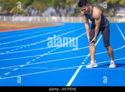 Junger Mann, der während der Behandlung an plötzlichen Knie- und Beinschmerzen leidet Das Training im Stadion Stockfoto