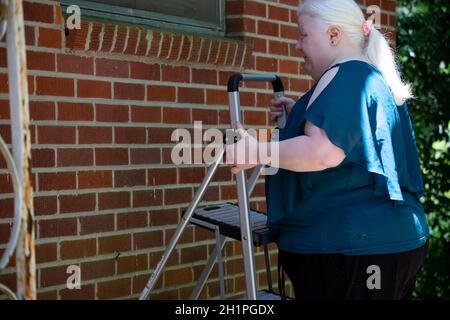 Albino Frau beim Aufstellen einer Leiter in der Nähe eines roten Ziegelwand für notwendige Reparaturen zu suchen Stockfoto