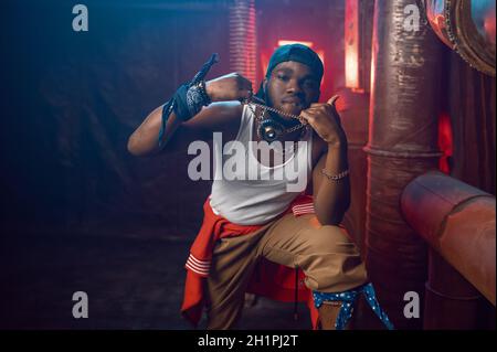 Stilvoller Rapper zeigt seinen Goldschmuck im Studio mit cooler Underground-Dekoration. Hip-Hop-Performer, Rap-Sänger, Breakdance Stockfoto