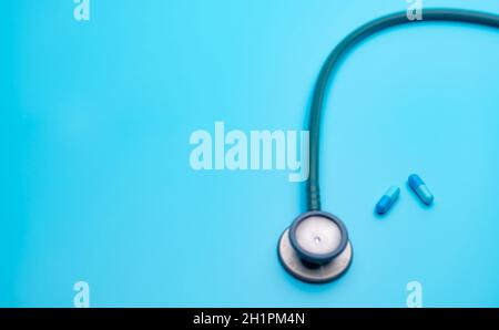 Blaue Kapseln und verschwommenes grünes Stethoskop auf blauem Hintergrund mit Kopierraum. Health Check. Kardiologische Ausrüstung für den Herzschlagtest. H Stockfoto