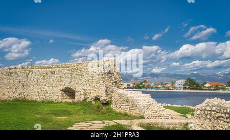 Zerstörte Mauer oder Festung, die Nin Dorf mit Blick auf moderne Bezirk und Gebirge der Dinarischen Alpen umgeben war der Hintergrund, Kroatien Stockfoto