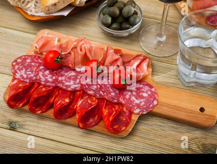 Spanische leckere Gerichte, die Würstchen und Schinken mit Tomaten am Holzschreibtisch schneiden Stockfoto