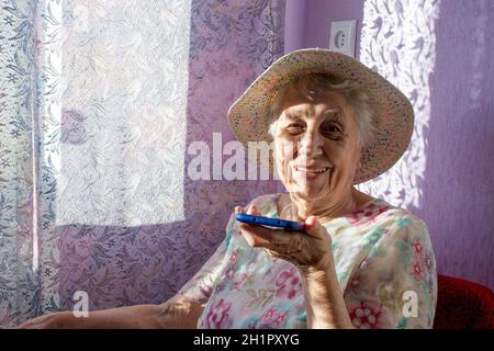 Charmante ältere Frau in rechteckiger, schwarz umrandter Brille mit Spracherkennungsfunktion auf dem Handy. Moderne ältere weibliche Holding elektronische gad Stockfoto