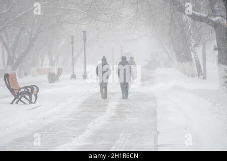 Eine schneebedeckte Straße mit Menschen in einem Sturm, Schneesturm oder Schneefall Im Winter bei schlechtem Wetter in der Stadt.Extreme Winterwetter Bedingungen im Norden.PE Stockfoto