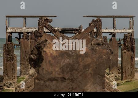 Blick auf Zerbrochene alte Struktur Überreste von Pier im Meer. Kleine Welle krachend in die texturierten rostigen Pierpfosten. Stockfoto