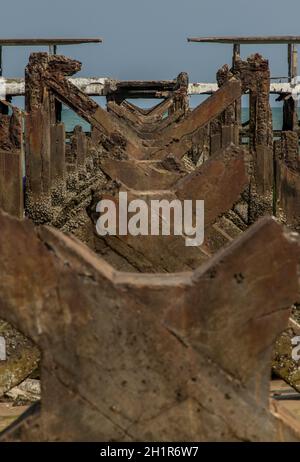 Blick auf Zerbrochene alte Struktur Überreste von Pier im Meer. Kleine Welle krachend in die texturierten rostigen Pierpfosten. Stockfoto