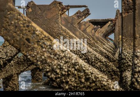 Blick auf Zerbrochene alte Struktur Überreste von Pier im Meer. Kleine Welle krachend in die texturierten rostigen Pierpfosten. Stockfoto