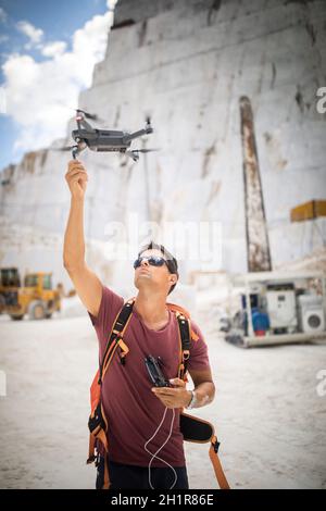 Junger Mann, der seine Drohne fliegt, nimmt Luftaufnahmen von einem Ort auf Stockfoto