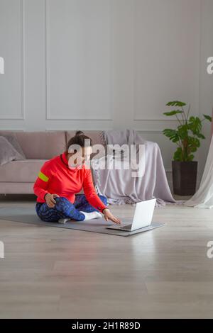 Eine Frau mittleren Alters mit Kopfhörern bereitet sich auf das Training im Internet vor. Sie sucht nach Tutorials für Yoga- oder Pilates-Trainingsvideos. Vertikales Foto. Stockfoto