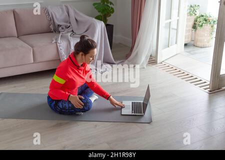 Eine Frau mittleren Alters mit Kopfhörern bereitet sich auf das Training im Internet vor. Sie sucht nach Online-Tutorials für Yoga- oder Pilates-Übungsvideos. Stockfoto