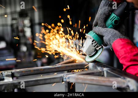 Schweißer verwendete Schleifstein auf Stahl in der Fabrik mit Funken, Schweißprozess in der Industriewerkstatt, Hände mit Instrument im Rahmen. Stockfoto