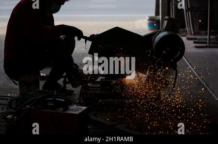 Schweißer verwendete Schleifstein auf Stahl in der Fabrik mit Funken, Schweißprozess in der Industriewerkstatt, Hände mit Instrument im Rahmen. Stockfoto