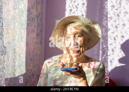 Charmante ältere Frau in rechteckiger, schwarz umrandter Brille mit Spracherkennungsfunktion auf dem Handy. Moderne ältere weibliche Holding elektronische gad Stockfoto