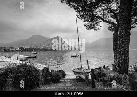 Boote und Bäume am Luganersee, Berg Monte Bre im Hintergrund. Schwarzweiß-Fotografie. Stockfoto