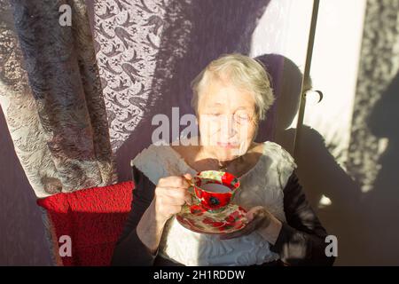 Ältere Frau genießt eine Tasse Tee oder Kaffee zu Hause sonnigen Hintergrund Stockfoto