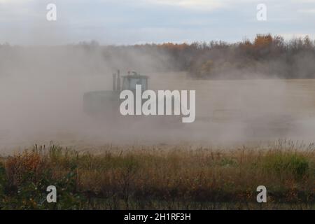 BONNYVILE, ALBERTA, KANADA - 10. SEPTEMBER 2020: Ein lokaler Landwirt im John Deere Traktor arbeitet in einer Staubwolke, während er ein geerntetes Feld gräbt. Stockfoto