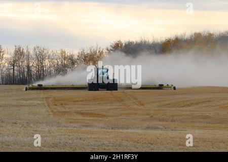 BONNYVILE, ALBERTA, KANADA - 10. SEPTEMBER 2020: Ein lokaler Landwirt im John Deere Traktor arbeitet vor einer Staubwolke, während er ein geerntetes Feld begrabt. Stockfoto