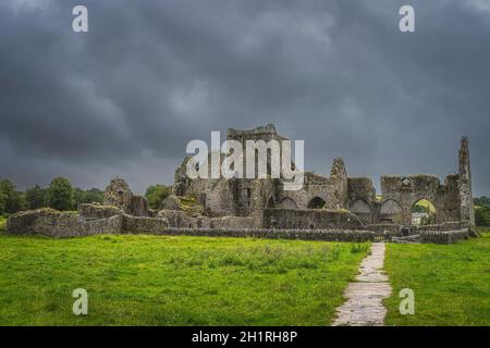 Fußweg zu den alten Ruinen der Hore Abbey mit dunklem, dramatischem Sturmhimmel. Das Hotel liegt neben dem Schloss Rock of Cashel, County Tipperary, Irland Stockfoto