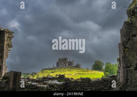 Blick durch alte Ruinen der Hore Abbey Mauern auf Rock of Cashel Burg mit dunklen dramatischen Sturmhimmel im Hintergrund, Grafschaft Tipperary, Irland Stockfoto