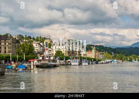 Luzern, Schweiz - 24. Mai 2016: Grand Hotel National und Gebäude entlang dem Vierwaldstättersee, Menschen in Booten auf dem See bei bewölktem Himmel. Luzern ist Stockfoto