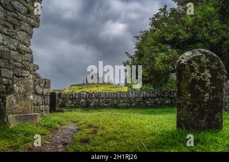 Blick durch alte Ruinen der Hore Abbey und Grabstein auf der Burg Rock of Cashel mit dunklem, dramatischem Sturmhimmel im Hintergrund, Grafschaft Tipperary, Irland Stockfoto