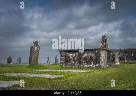 Altes keltisches Kreuz, Grabstein und Gräber mit dramatischem Sturmhimmel im Hintergrund in Rock of Cashel, Irland Stockfoto