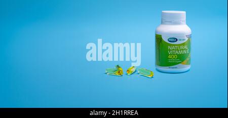 CHONBURI, THAILAND-JANUARY 31, 2021 : Mega We care Natural Vitamin E 400 IU in PP-Plastikflasche und vier weiche Gelatine Kapsel auf blauem Hintergrund. Pro Stockfoto