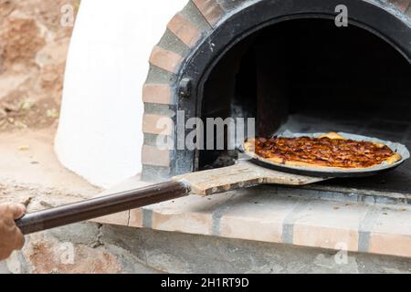Pizza aus einem weiß lackierten, handgefertigten Holzofen, der auf der Außenseite gebaut wurde Stockfoto