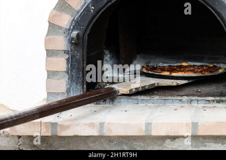 Pizza aus einem weiß lackierten, handgefertigten Holzofen, der auf der Außenseite gebaut wurde Stockfoto