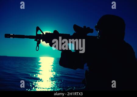 Moderne Armee Infanterie Soldat, Küstenwache Sturmgewehr mit Kollimator Anblick in der Nacht anvisieren. Spezialoperationen Forces Fighter Eingriffs en Stockfoto