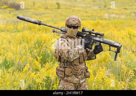 Soldat mit großem Scharfschützengewehr geht über blühendes Feld Stockfoto