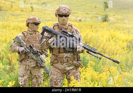 Zwei bewaffnete Soldaten der Spezialeinheiten mit Scharfschützengewehren Das blühende Feld Stockfoto