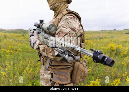 Soldat mit Scharfschützengewehr im blühenden grünen Feld Stockfoto