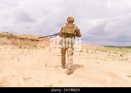 Spezialwehrsoldat in Tarnung mit Gewehr geht durch die Wüste Stockfoto