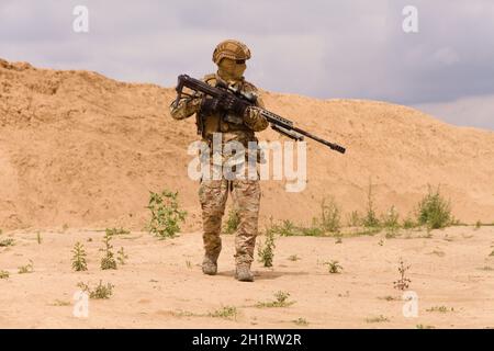 Ausgerüsteter und bewaffneter Spezialeinsatzsoldat mit Gewehr in der Wüste während der Militäroperation. Stockfoto