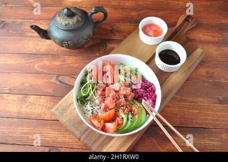 Thunfisch-Schüssel mit Kristallnudeln, frischem Rotkohl, Avocado, Kirschtomaten. Food Concept Poke Bowl auf Holzhintergrund. Bio-Lebensmittel. Frisches Meer Stockfoto