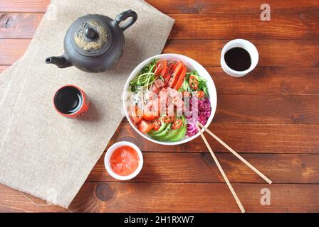 Thunfisch-Schüssel mit Kristallnudeln, frischem Rotkohl, Avocado, Kirschtomaten. Food Concept Poke Bowl auf Holzhintergrund. Bio-Lebensmittel. Frisches Meer Stockfoto