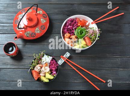 Bio-Lebensmittel. Rezept für frische Meeresfrüchte. Zwei frische Schüsseln mit Lachs, Garnelen, Reis, Rotkohl, Avocado, Kirschtomaten und Rettich sprießen auf Holz Stockfoto
