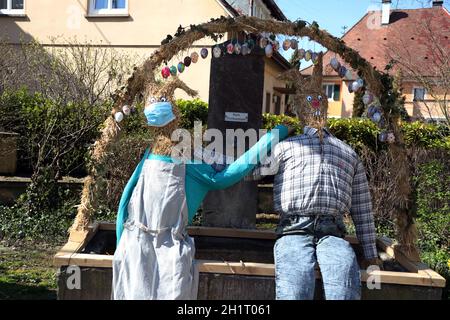 Mund- und Nasenschutz und mit Abstand - dies gilt auch für diese beiden Stroh-Osterhasen am Brunnen von Hausen an der Möhlin Themenbild Medizin - C Stockfoto