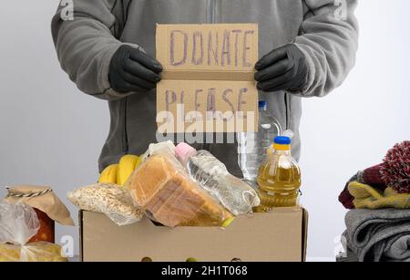 Mann hält ein Blatt Papier mit einem Schriftzug spenden bitte und sammelt Lebensmittel, Früchte und Dinge in einem Karton, um die Bedürftigen und die Armen, die zu helfen Stockfoto