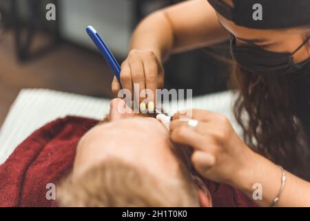 Barber Frau rasiert Bart mit einem Rasiermesser. Friseurausrüstung. Selektiver Fokus. Master in Gesichtsmaske. Stockfoto