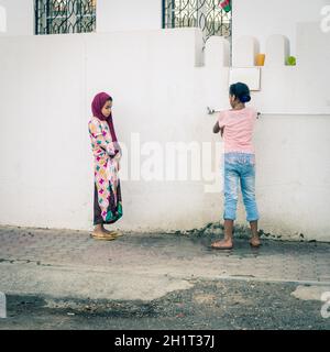 Maskat, Oman, 3. Dezember 2016: Zwei Mädchen an einem Wasserzapfen vor einer Moschee in der Altstadt von Maskat, Oman Stockfoto