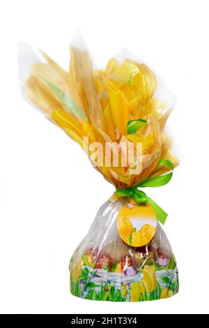 Osterschmuck. Eine dekorative Ostergeschenk-Box aus Folie oder Zellophan mit Schleife und leerem Papieranhänger gefüllt mit Schokoladenbonbons, isoliert auf einem W Stockfoto