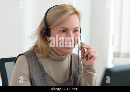 Eine Geschäftsfrau, die mit einem Headset und einer Kamera vor einem Computer sitzt, kommuniziert per Video. Nahaufnahme im Hochformat. Stockfoto