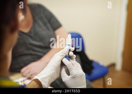 Weibliche GP-Chirurgie Krankenschwester trägt Handschuhe macht sich bereit, eine Injektion an eine weibliche Patientin in einer NHS-Chirurgie zu verabreichen Stockfoto
