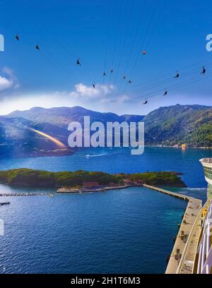 Menschen, die auf der karibischen Insel Labadee auf Haiti mit hoher Zipline fliegen. Die ariale Ansicht vom Abstieg des abstrakten Kreuzschiffs auf caribbean Haiti auf sonniger Höhe Stockfoto