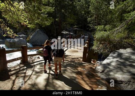 Menschen, die über eine Fußgängerbrücke über den Merced River auf dem Mist Trail, Yosemite National Park, Kalifornien, USA, laufen Stockfoto