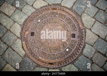 Runde Eiserne Luke für Kanalisation auf Kopfsteinpflaster in Dresden, Deutschland. Stahlkanal auf dem Bürgersteig. Stockfoto