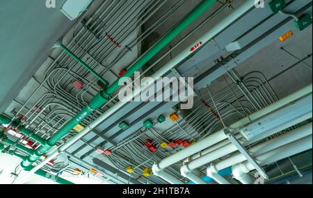 Elektrisches Rohrsystem und verzinktes Stahlrohr mit Elektrokabel an der Decke installiert. PVC-Kunststoffrohr des Abflusssystems und sauberes Wasser auf der Schale Stockfoto