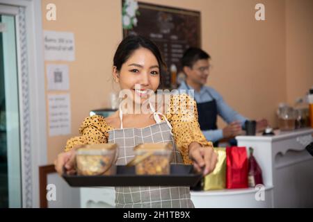 Lächelnde Frauen, die als Inhaber kleiner Unternehmen im Café Kekse hielten. Stockfoto